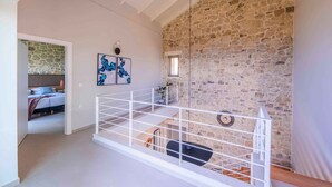 A loft-style room with a stone wall, a white railing, and a bed with a view. - Villa Mare I Free Heated Pool Infinite Blue (Kissamos)