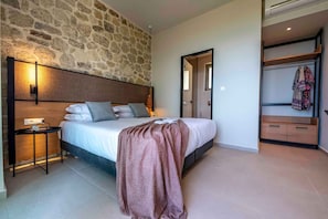 A bedroom with a stone wall, a bed with pillows, a bedside table, and a wardrobe. - Villa Mare I Free Heated Pool Infinite Blue (Kissamos)