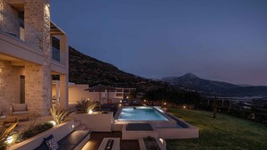 A modern outdoor pool area with a stone building, seating, and a view of a mountainous landscape. - Villa Mare I Free Heated Pool Infinite Blue (Kissamos)