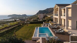 A resort with a swimming pool, lounge chairs, and a view of the sea and hills. - Villa Mare I Free Heated Pool Infinite Blue (Kissamos)
