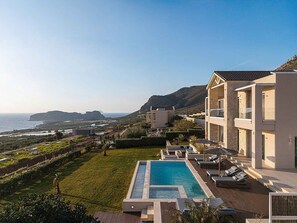 A resort with a swimming pool, lounge chairs, and a view of the sea and hills. - Villa Mare I Free Heated Pool Infinite Blue (Kissamos)