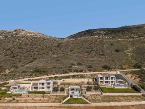 A hillside property with modern houses, a swimming pool, and a clear view of the surrounding landscape.