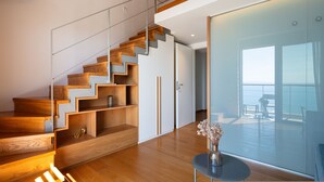 Un intérieur moderne avec un escalier en bois, une porte vitrée donnant sur un balcon et une petite table surmontée d’un vase.