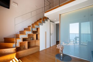 Un intérieur moderne avec un escalier en bois, une porte vitrée donnant sur un balcon et une petite table surmontée d’un vase.