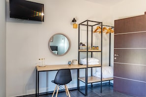 Ein gemütliches Hotelzimmer mit einem Bett, einem Schreibtisch mit Stuhl, einem Kleiderschrank, einem Spiegel und einem Fernseher an der Wand.
