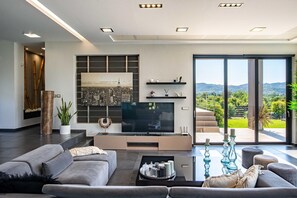 Ein modernes Wohnzimmer mit Flachbildfernseher, bequemen Sitzgelegenheiten, einem Couchtisch und einem großen Fenster mit schöner Aussicht.
