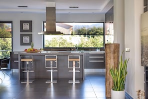 Cocina moderna con una isla grande, taburetes de bar y vistas a la vegetación.