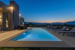 Una piscina con sillones de descanso y un edificio moderno con iluminación.