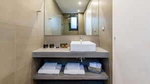 Une salle de bain moderne avec un grand miroir, un lavabo blanc et des serviettes soigneusement pliées sur une étagère.