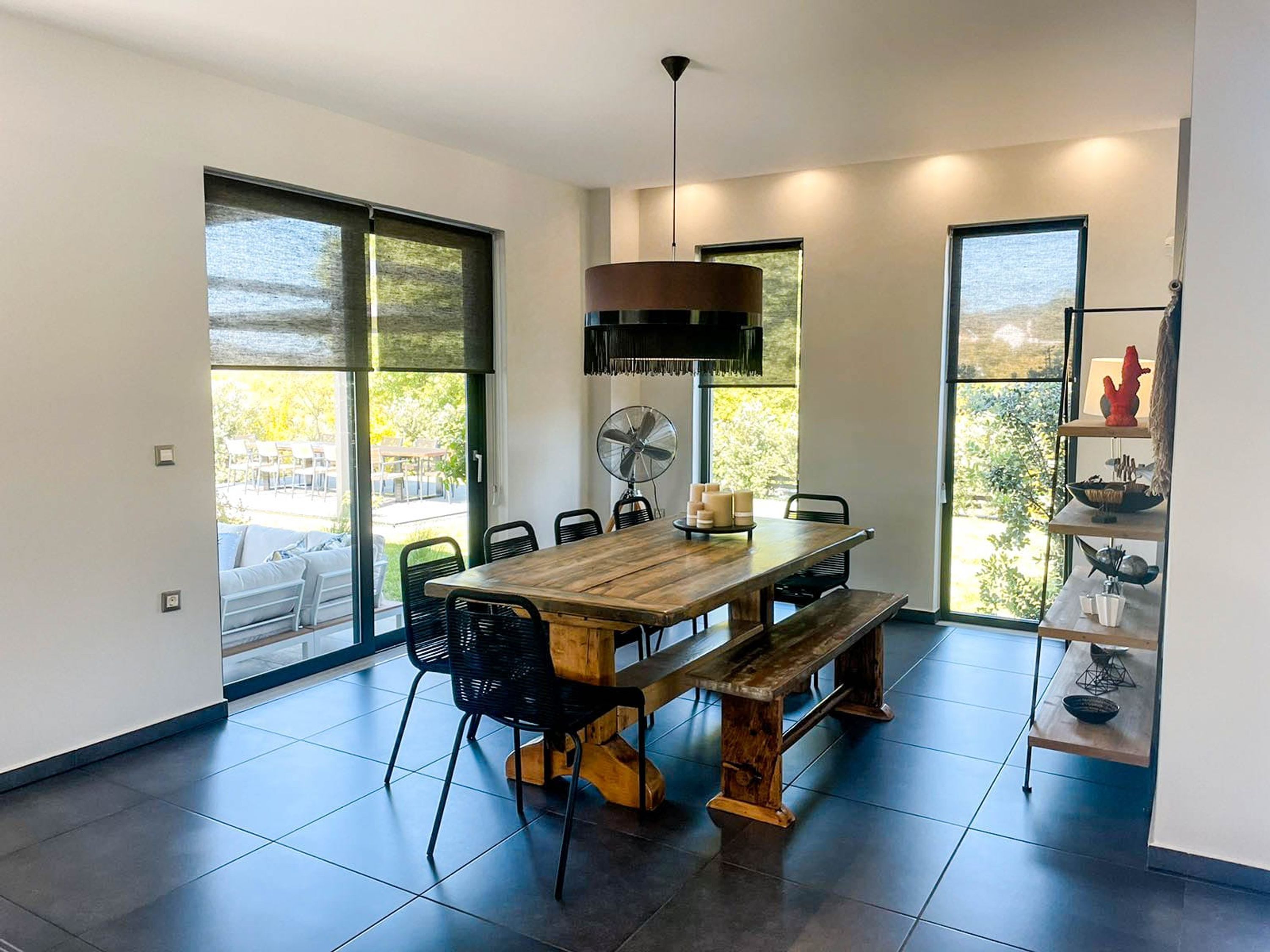 A modern dining area with a wooden table, black chairs, a fan, and a view of the outdoors.