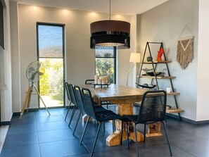 Un comedor con una mesa de madera, sillas negras, un ventilador de pie y una lámpara colgante.