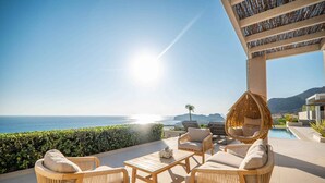 Un área de estar al aire libre iluminada por el sol, con mobiliario de mimbre y vistas al mar.