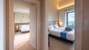 Habitación de hotel con pared de piedra, cama con detalles en azul y vista al mar.