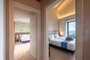A hotel room with a stone wall, a bed with a blue accent, and a view of the sea.