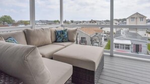 Un balcon abrité avec un canapé d’angle beige, de grandes fenêtres offrant une vue sur des immeubles résidentiels et une route.