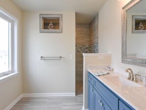 A bathroom with a large mirror, a towel rack, and a sink with blue cabinets. - Seas The Day says it all. 4 BR house on the canal! (Selbyville)