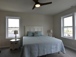 A bedroom with a bed, two bedside lamps, a ceiling fan, and large windows. - Seas The Day says it all. 4 BR house on the canal! (Selbyville)