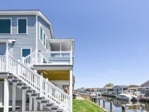 A two-story house with a wooden deck and a staircase leading to a balcony. - Seas The Day says it all. 4 BR house on the canal! (Selbyville)