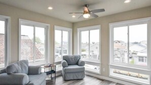 Une pièce spacieuse avec de grandes fenêtres, un ventilateur de plafond et un canapé gris.