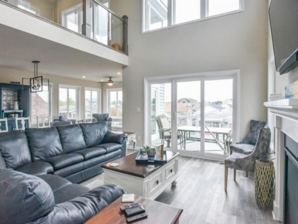 A spacious living room with a black leather sofa, a coffee table, and a dining area with chairs. - Seas The Day says it all. 4 BR house on the canal! (Selbyville)