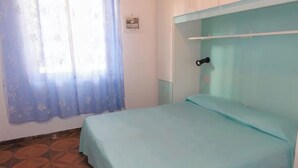 Ein Zimmer mit einem Bett, einem Fenster mit Vorhang und einem Fliesenboden.