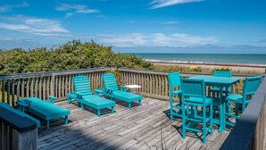 Een houten terras met turquoise buitenmeubilair met uitzicht op een strand.