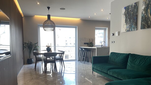 A modern living room with a green sofa, a dining table with chairs, and a kitchen area in the background. - Apartment 20 meters from the sea luxurious modern with all amenities (Tas-Sliema)