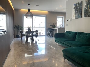 A modern living room with a green sofa, a dining table with chairs, and a kitchen area in the background. - Apartment 20 meters from the sea luxurious modern with all amenities (Tas-Sliema)