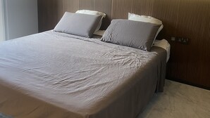 A modern hotel room with a large bed, a headboard with vertical lines, and a bedside table with a lamp. - Apartment 20 meters from the sea luxurious modern with all amenities (Tas-Sliema)