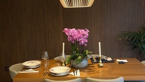 A dining area with a wooden table, four chairs, a vase with pink flowers, and a hanging light fixture. - Apartment 20 meters from the sea luxurious modern with all amenities (Tas-Sliema)