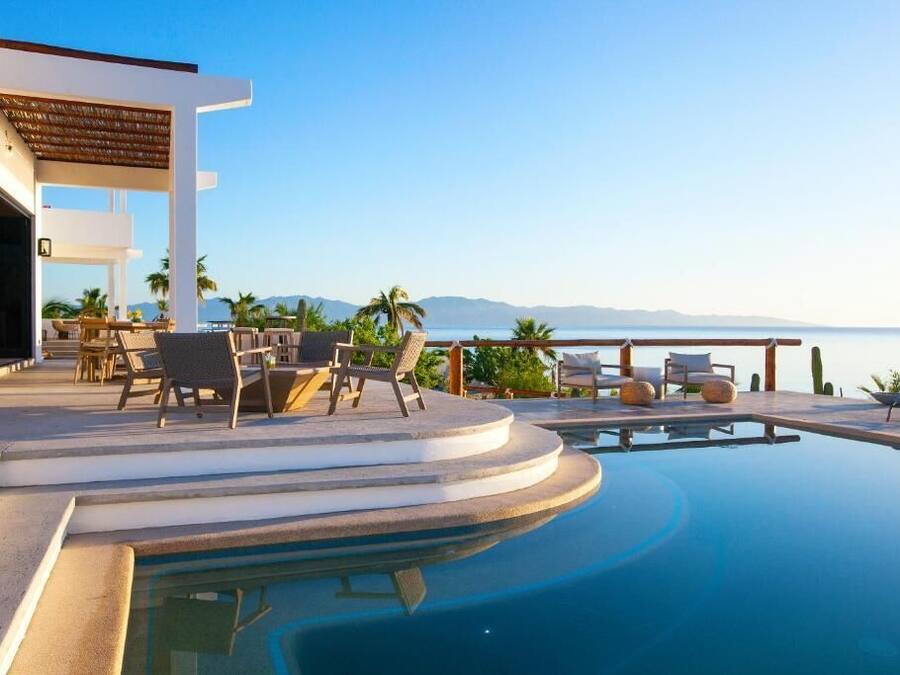 Un área de piscina moderna con sillones de descanso y vistas al mar.