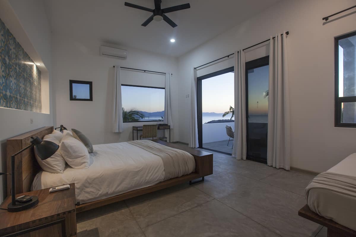 Ein Schlafzimmer mit Bett, Schreibtisch, Stuhl, Deckenventilator und Meerblick.