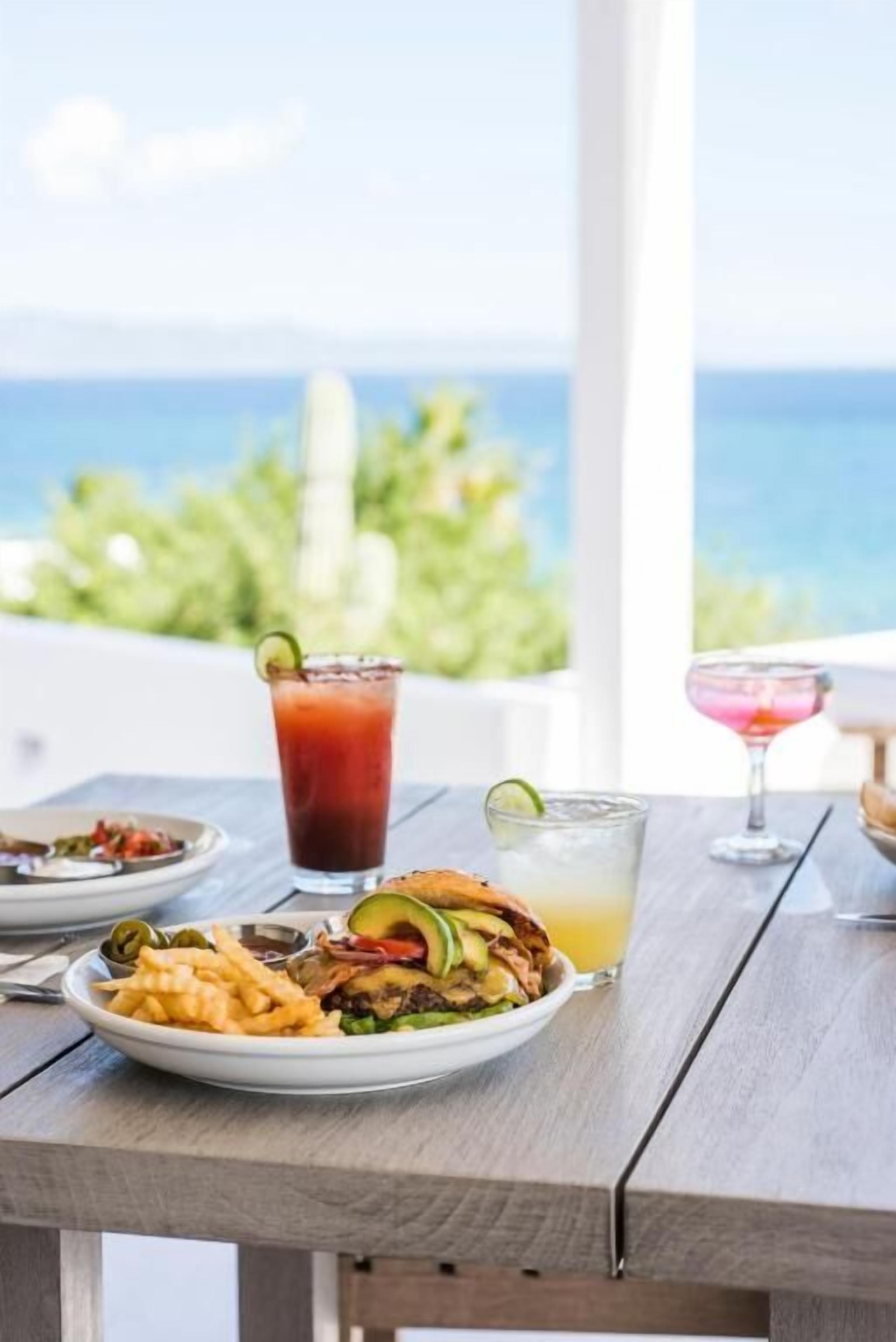 Une table dressée avec un repas et des boissons, offrant une vue panoramique sur l’océan.