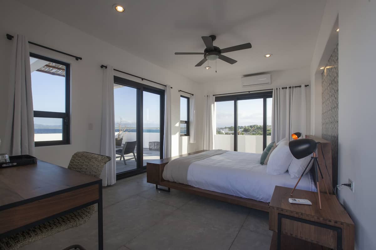 Ein modernes Schlafzimmer mit einem großen Bett, einem Schreibtisch und einem Balkon mit Meerblick.
