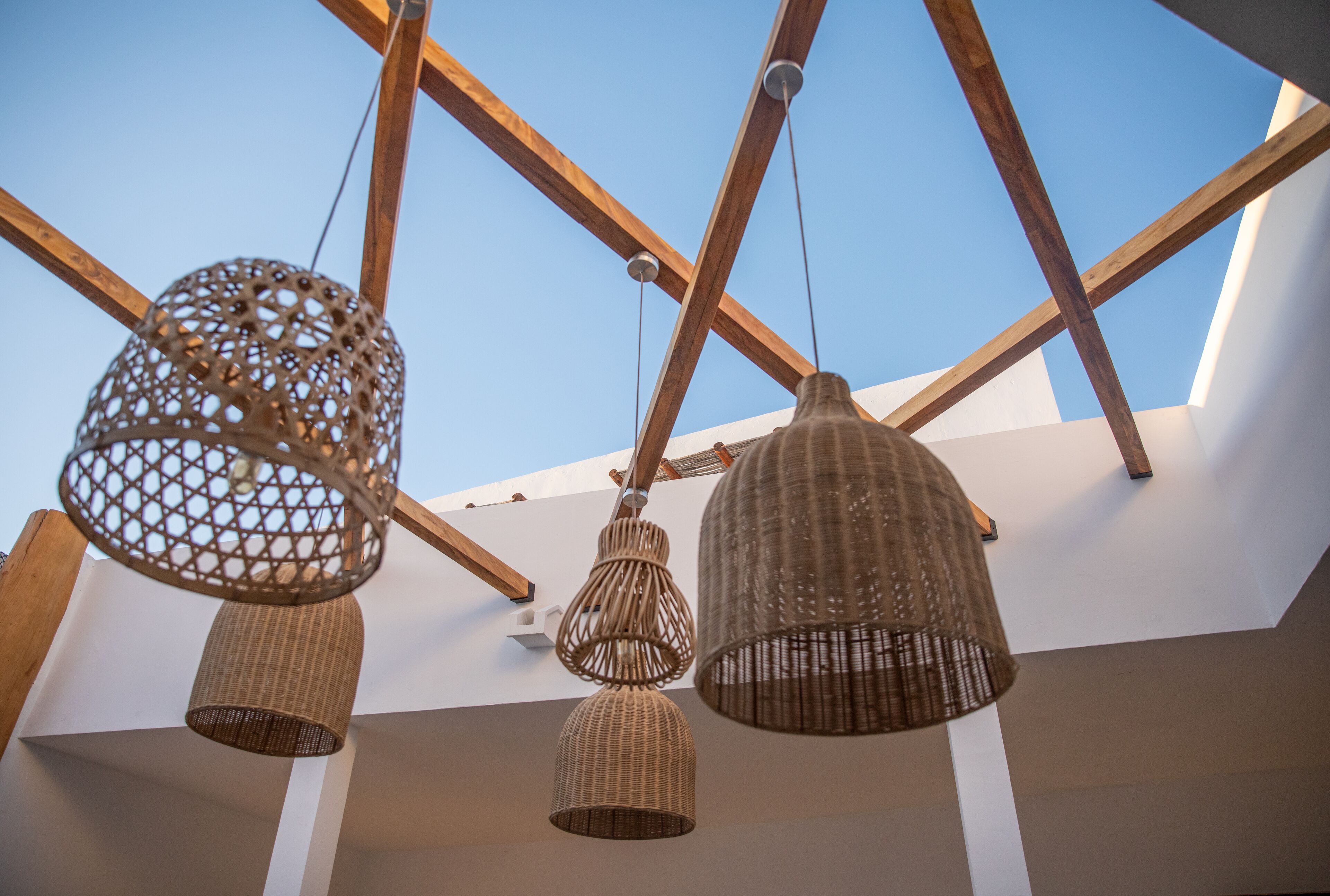 Three wicker pendant lights hanging from a wooden ceiling structure.