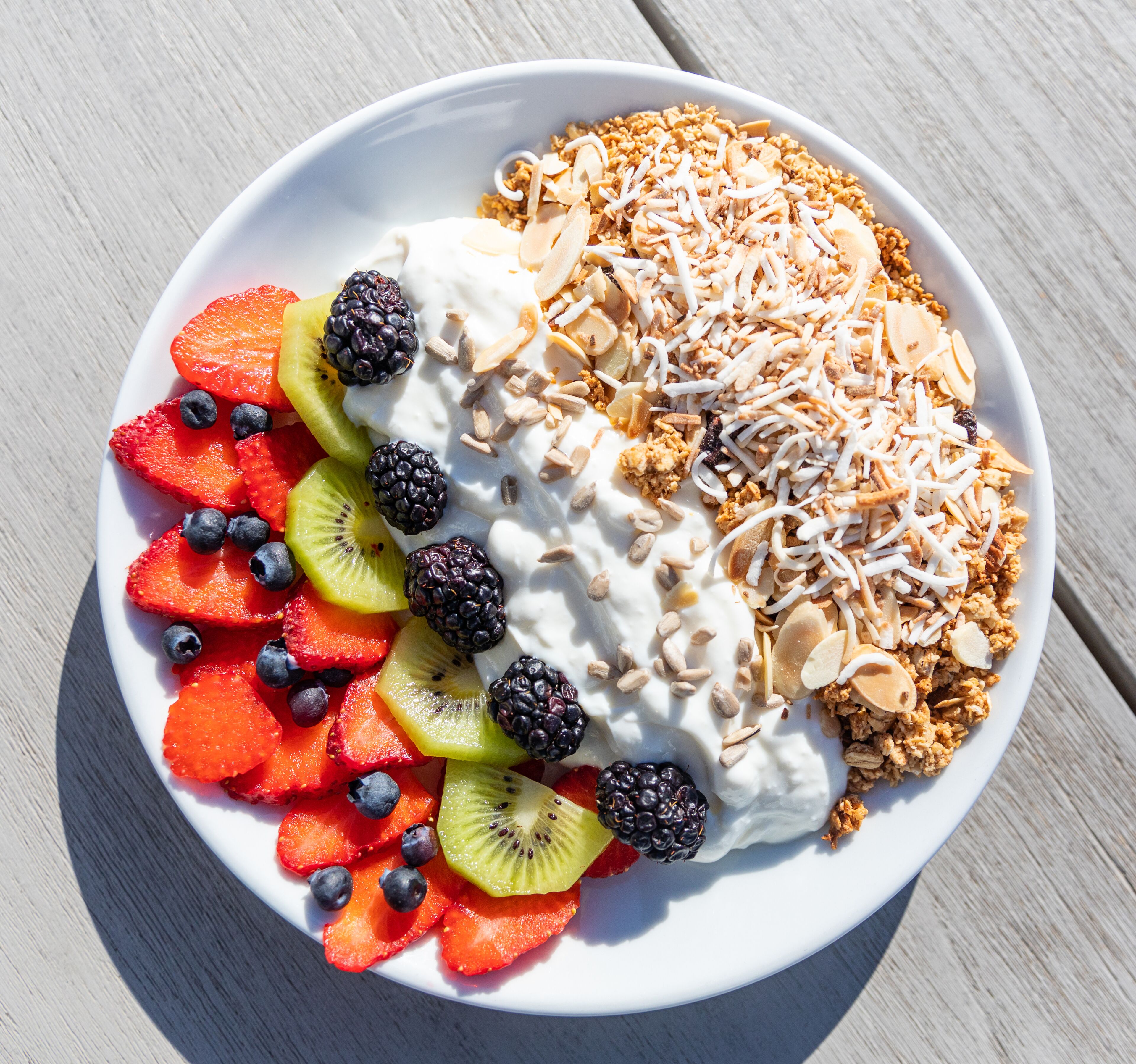 Un bol de salade de fruits, accompagné de yaourt et de granola, sur une table en bois.