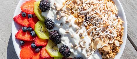 Un bol de salade de fruits, accompagné de yaourt et de granola, sur une table en bois.
