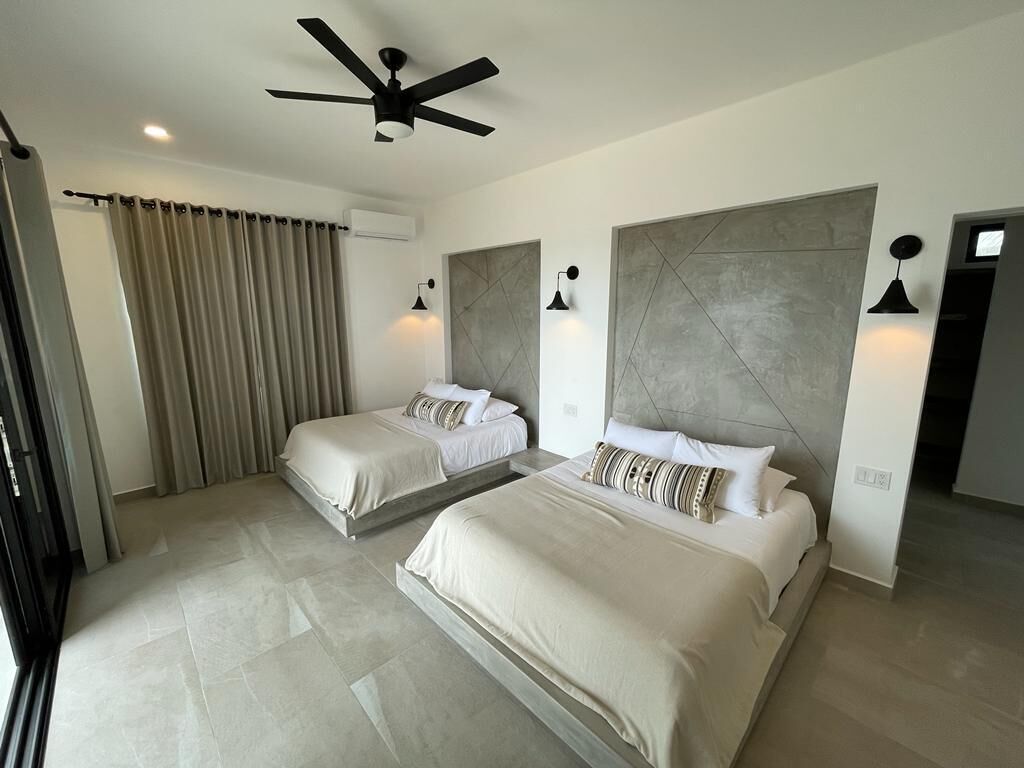 Een moderne hotelkamer met twee bedden, een plafondventilator en een groot raam met gordijnen.