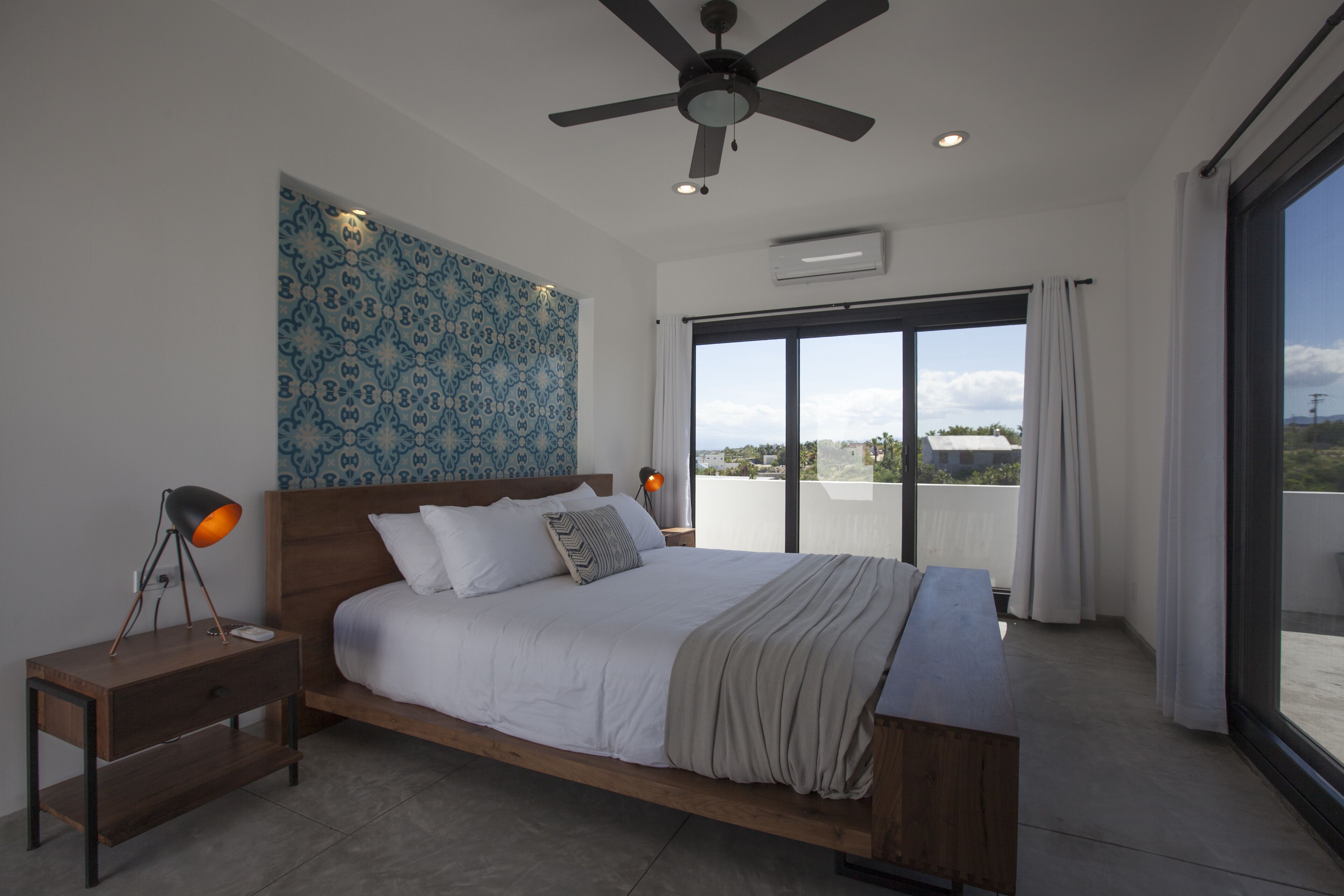 A modern bedroom with a large bed, a ceiling fan, and a view of the city through a large window.