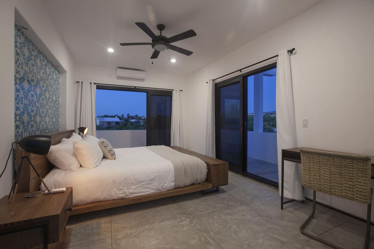 Ein modernes Schlafzimmer mit einem großen Bett, einem Deckenventilator und Blick ins Freie.