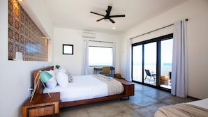 Un dormitorio moderno con una cama grande, un ventilador de techo y vista al océano a través de una puerta corrediza de vidrio.