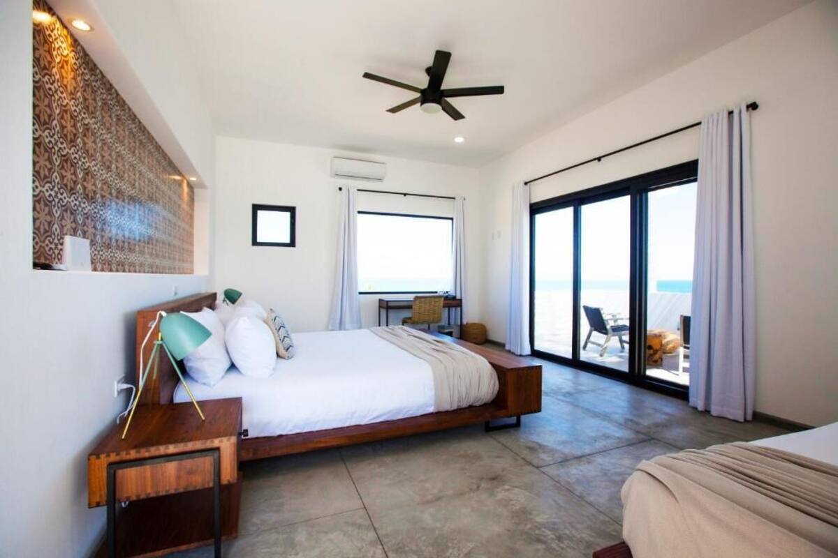 Ein modernes Schlafzimmer mit einem großen Bett, einem Deckenventilator und Meerblick durch eine Glastür.