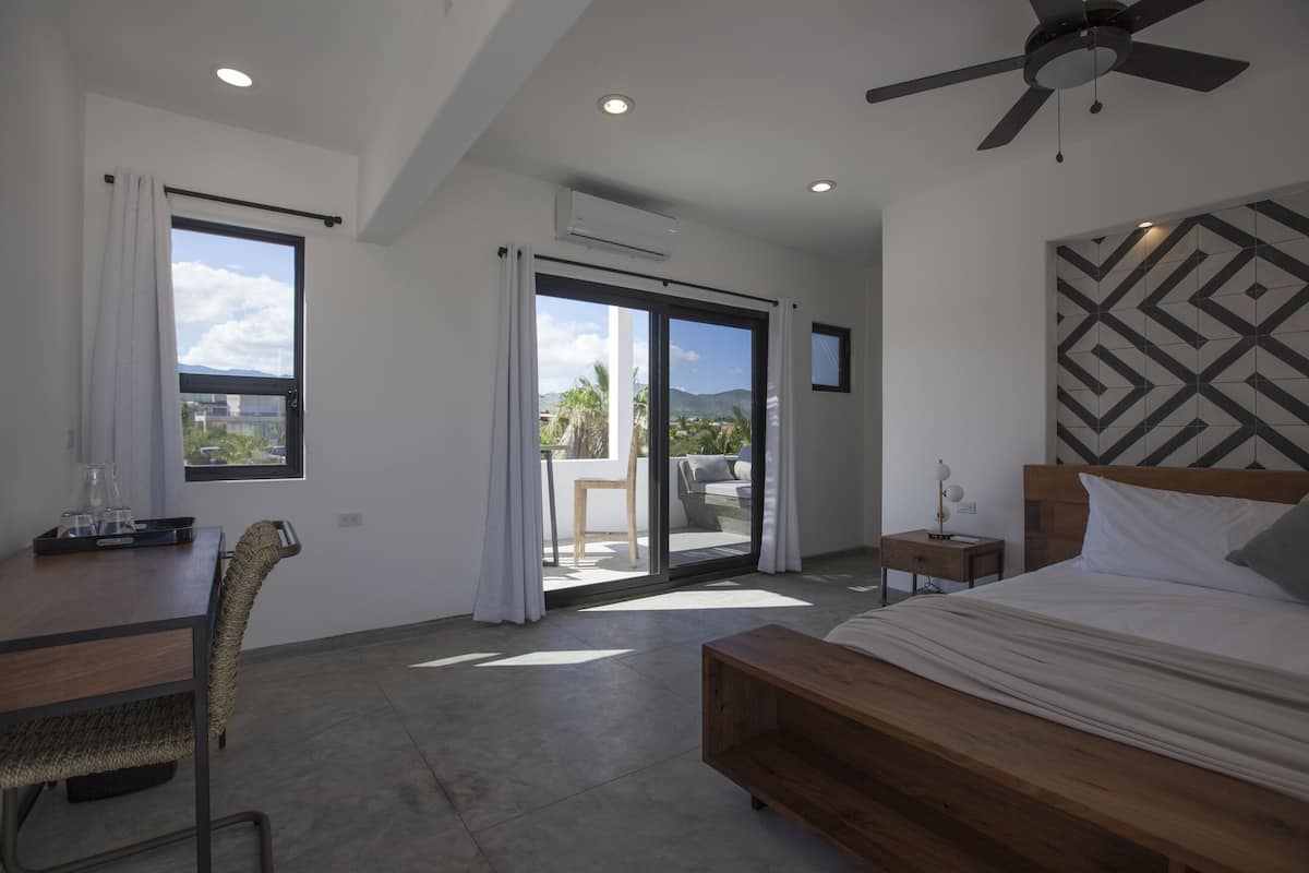 Ein modernes Schlafzimmer mit Bett, Schreibtisch und Stuhl. Ein Balkon bietet einen Blick ins Freie.