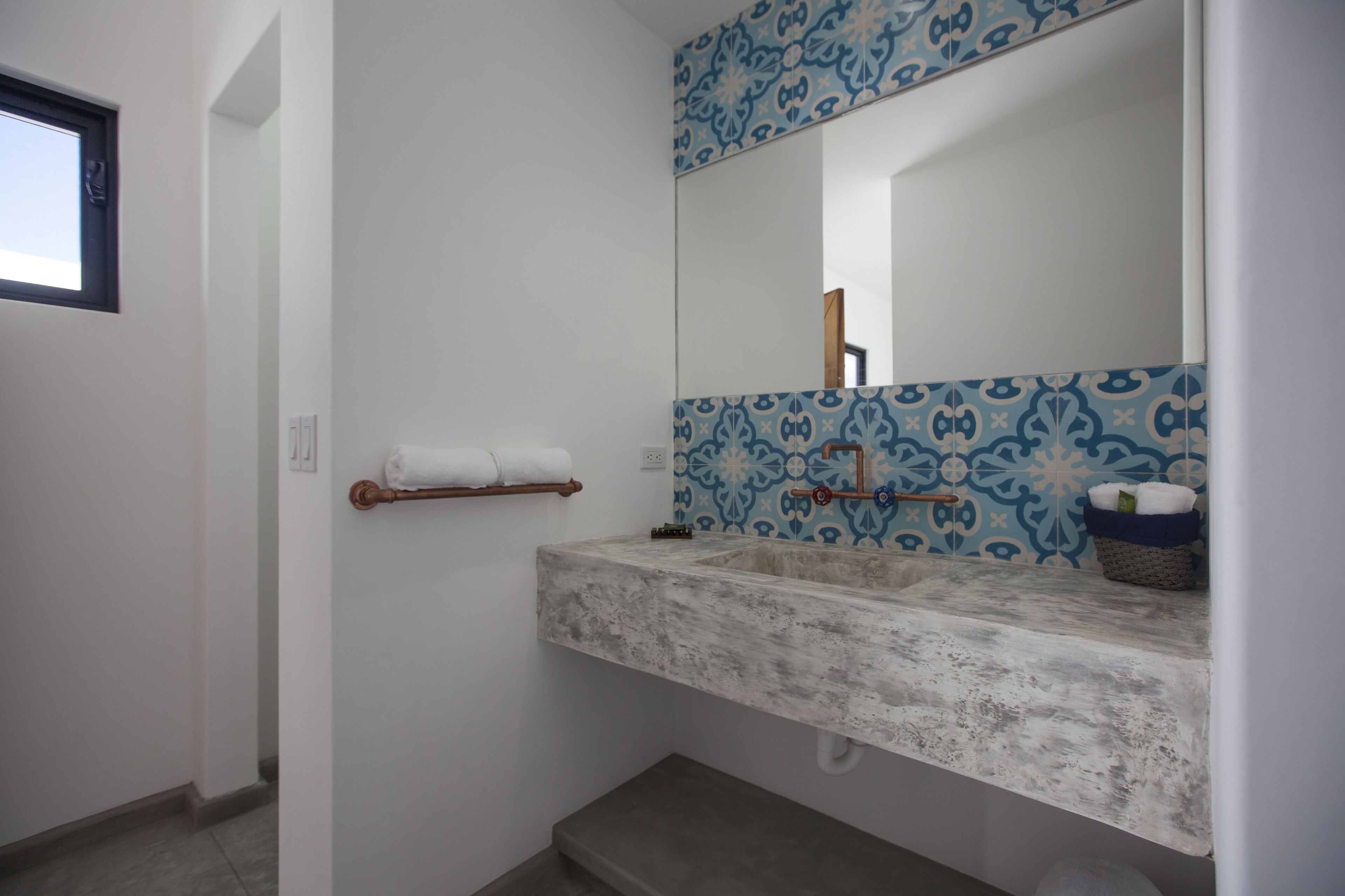 A bathroom with a white sink, blue patterned tiles, a towel rack, and a mirror.