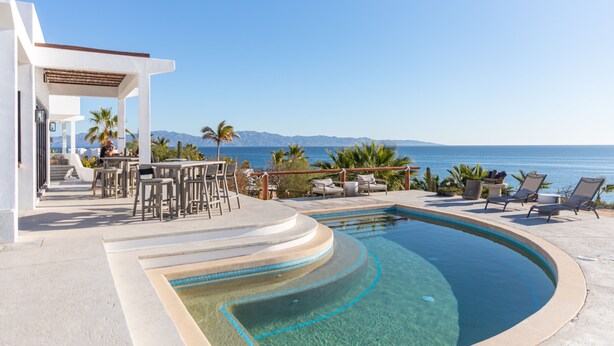 Zona de piscina con vistas al mar, mobiliario exterior y una pérgola.