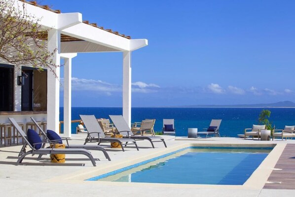 Un área junto a la piscina con sillas de descanso y vista al mar.