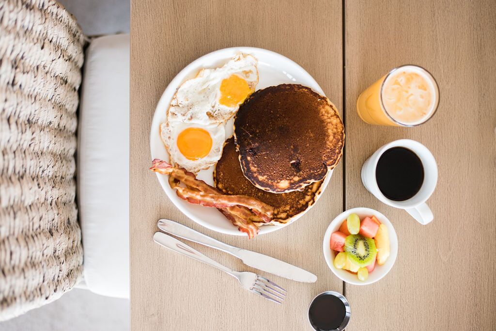 A breakfast plate with pancakes, eggs, bacon, and a side of fruit and coffee.