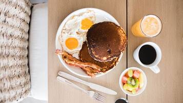 A breakfast plate with pancakes, eggs, bacon, and a side of fruit and coffee.