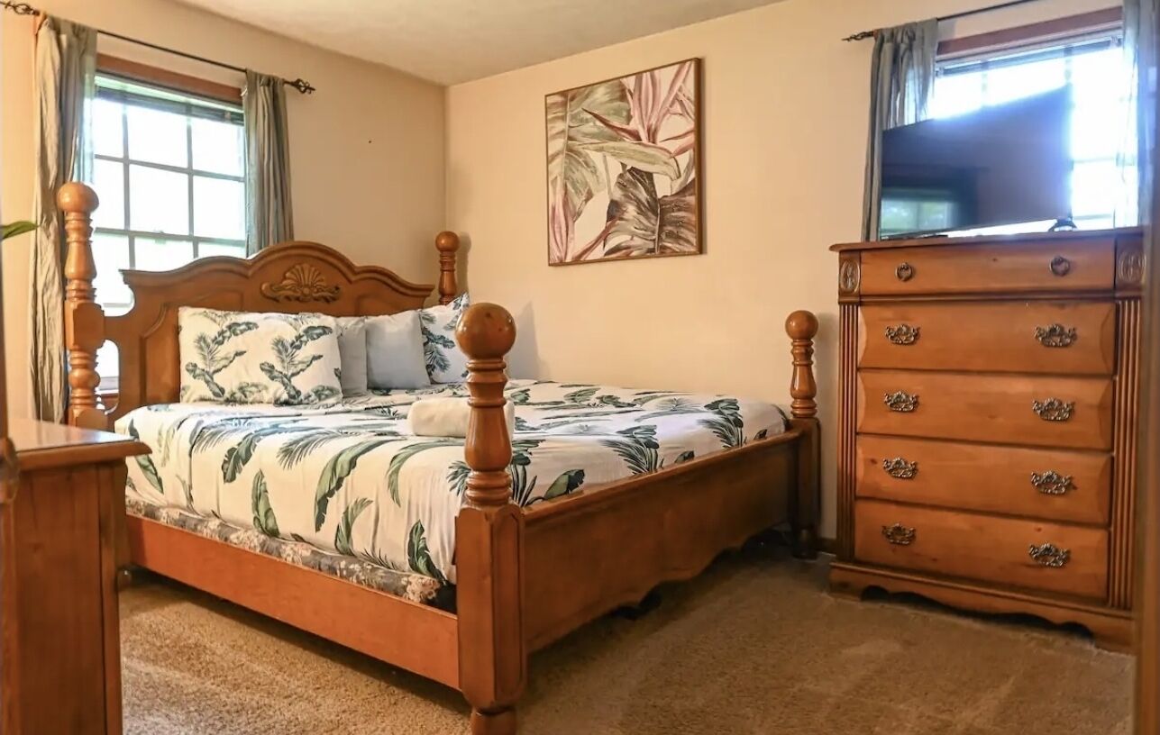 A bedroom with a wooden bed, a dresser, and a painting on the wall.