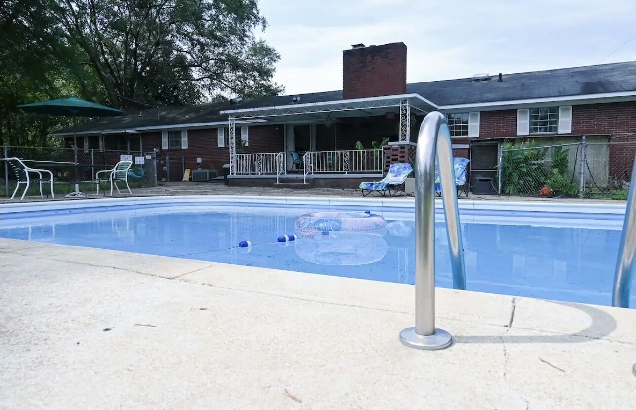 A swimming pool with a covered patio area, lounge chairs, and a fenced deck.